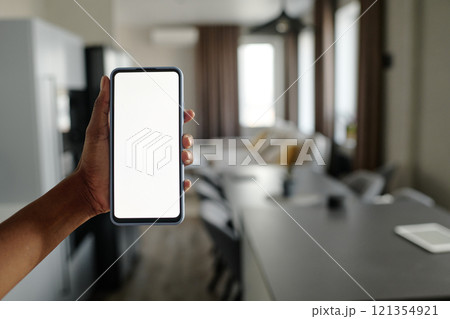 Unrecognizable female hand holding smartphone, blurred apartment in background 121354921