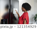 Side view of African American housewife sorting out fridge app on white display 121354929
