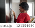 Medium close up of African American woman in red knitted shirt seeing into fridge application 121354930