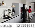 Clean minimalist kitchen area with woman standing next to smart fridge and using control system 121354932