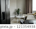 Smart fridge next to dining table in kitchen zone, spacious and minimalist style living room with beige sofa and wooden coffee table 121354938