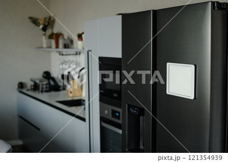 Black matte fridge with white tablet on its door in modern kitchen fully equipped with kitchen appliances 121354939