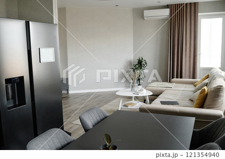 Modern dining area with graphite fridge and same colored table, light living room with comfortable couch and multicolored cushions 121354940