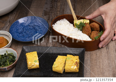 弁当箱にご飯やおかずを詰める手元 121357354