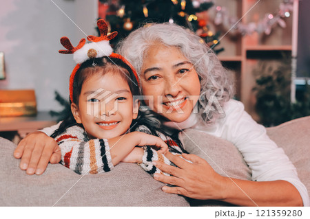 Happy family on Christmas morning. Affectionate grandmother and cheerful granddaughter open a holiday gift together at home Happy family on Christmas morning. Affectionate grandmother and cheerful granddaughter open a holiday gift together at home 121359280