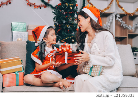 Merry Christmas and Happy Holidays. Cheerful mom and her cute daughter girl exchanging gifts. Parent and little child having fun near tree indoors. Merry Christmas and Happy Holidays. Cheerful mom and her cute daughter girl exchanging gifts. Parent and little child having fun near tree indoors. 121359333