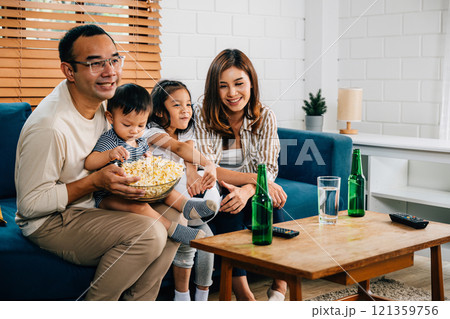 A happy family and their daughter enjoy watching football on TV at home, sharing moments of togetherness and excitement as they cheer and celebrate their team's success. 121359756