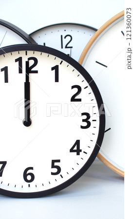 A composition of several analog clocks with black and white faces, overlapping to showcase a mix of styles, including black and wooden frames, against a plain white background. 121360073