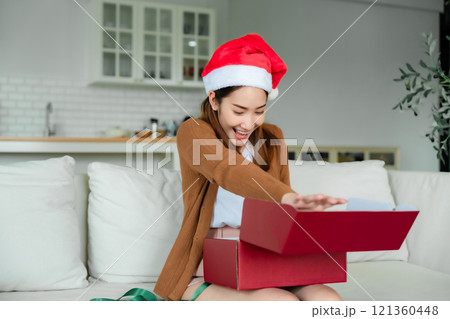 Young Asian woman wearing Christmas hat and opening a gift box Young Asian woman wearing Christmas hat and opening a gift box 121360448