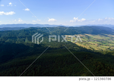 Aerial view of mountain hills covered with dense green lush woods on bright summer day. 121360786