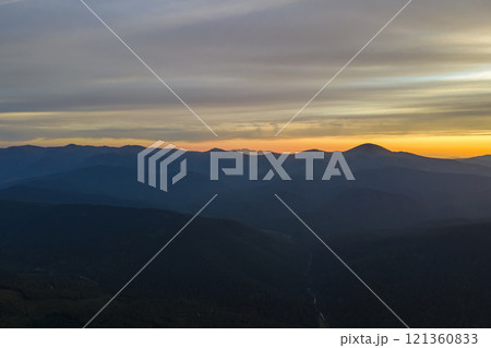 Aerial view of dark mountain hills with bright sunrays of setting sun at sunset. Hazy peaks and misty valleys in evening 121360833