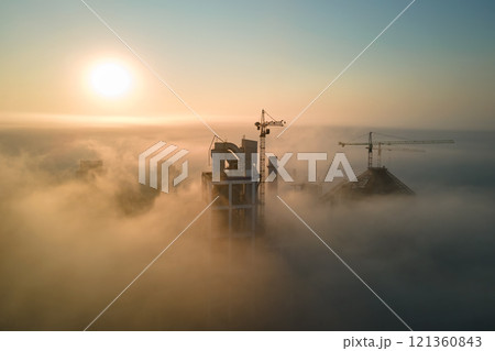 Aerial view of cement factory with high concrete plant structure and tower crane at industrial manufacturing site on foggy evening. Production and global industry concept. Aerial view of cement factory with high concrete plant structure and tower crane at industrial manufacturing site on foggy evening. Production and global industry concept. 121360843