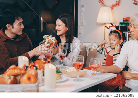 Portrait of Asian family exchanging presents during christmas at home. Attractive happy people holding gift box, celebrate holiday thanksgiving, xmas eve tradition in living room in house together. 121362099