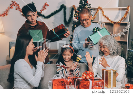 Portrait of Asian family exchanging presents during christmas at home. Attractive happy people holding gift box, celebrate holiday thanksgiving, xmas eve tradition in living room in house together. 121362103