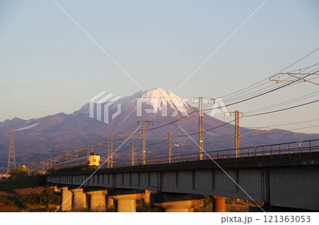 冠雪の大山の裾野に向かって日野川の橋梁を国鉄色381系特急やくも号リバイバル塗装車両が駆け抜ける光景 121363053