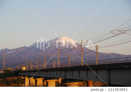 冠雪の大山の裾野に向かって日野川の橋梁を国鉄色381系特急やくも号リバイバル塗装車両が駆け抜ける光景 121363061
