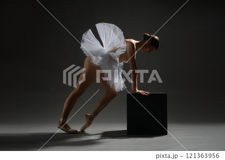 Ballerina gracefully posing with a black box in a studio setting Ballerina gracefully posing with a black box in a studio setting 121363956