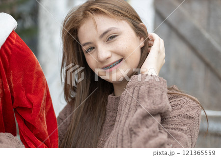 Portrait of young caucasian beautiful woman blond hair smiling in sweater with snow on Christmas Day. with braces. Happy girl in good mood smile showing teeth looking at camera. 121365559