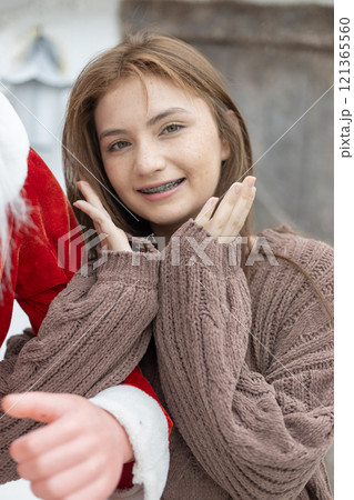 Portrait of young caucasian beautiful woman blond hair smiling in sweater with snow on Christmas Day. with braces. Happy girl in good mood smile showing teeth looking at camera. Portrait of young caucasian beautiful woman blond hair smiling in sweater with snow on Christmas Day. with braces. Happy girl in good mood smile showing teeth looking at camera. 121365560