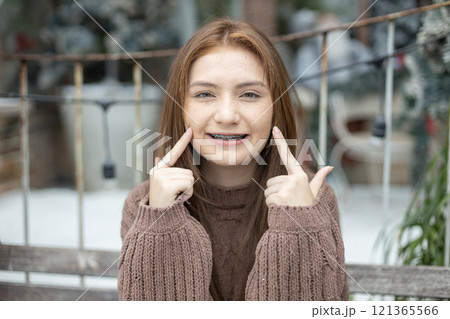Portrait of young caucasian beautiful woman blond hair smiling in sweater with snow on Christmas Day. with braces. Happy girl in good mood smile showing teeth looking at camera 121365566