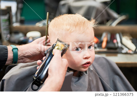 Barber using comb and shaver to cut hair. Professional hairdresser shaving little kid's nape. Close up. 121366375