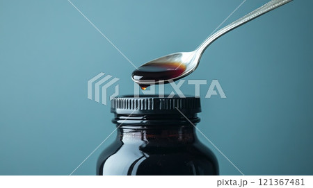Close-Up of Clear Cough Syrup Bottle with Spoon Dropping Liquid Against a Blue Background 121367481