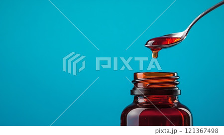 Close-Up of Clear Cough Syrup Bottle with Spoon on Bright Blue Background 121367498