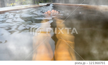 湯煙の立つ檜の露天風呂に入浴する男性の足 湯煙の立つ檜の露天風呂に入浴する男性の足 121368701