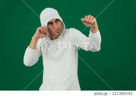 A man in a hoody trains boxing against a gray wall.  121369191