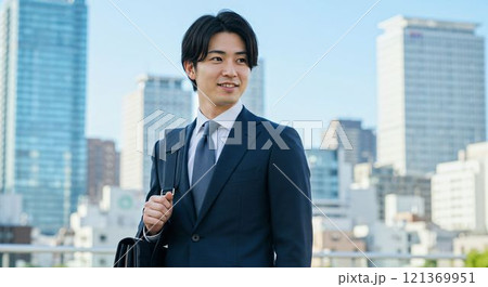 現代の都市風景でビジネスバッグを持つスーツ姿の若い日本人ビジネスマン 121369951