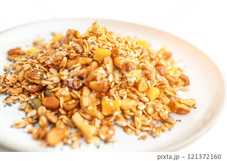 A bowl of granola with nuts and seeds on a white plate. The granola is a mix of different types of grains and nuts, and it looks like a healthy snack. 121372160