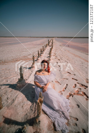 Woman Pink Salt Lake Photo Shoot - A woman in a white dress poses on a wooden boardwalk in a pink salt lake. 121372187
