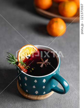 Mulled wine with orange, cinnamon and rosemary in a cup on a dark background with tangerines. Mulled wine with orange, cinnamon and rosemary in a cup on a dark background with tangerines. 121373087