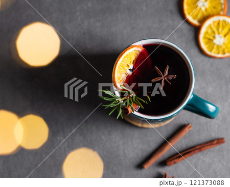 Mulled wine with orange, cinnamon and rosemary in a cup on a dark background with blur garlands. 121373088