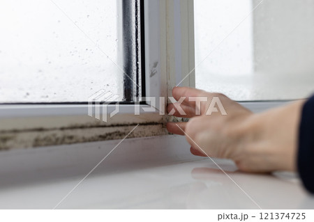 Woman touching the wet window with black mouldy fungus. Closeup. Woman touching the wet window with black mouldy fungus. Closeup. 121374725