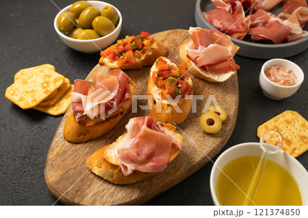 Italian sandwiches bruschetta with olives, bran bread, cherry tomatoes, prosciutto on wooden cutting board, dark black background surface Italian sandwiches bruschetta with olives, bran bread, cherry tomatoes, prosciutto on wooden cutting board, dark black background surface 121374850