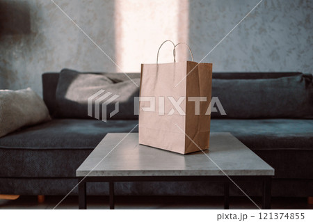 Disposable bag of kraft paper with products left by courier of food delivery service on a table at home. Copy space. Kraft design. Disposable bag of kraft paper with products left by courier of food delivery service on a table at home. Copy space. Kraft design. 121374855