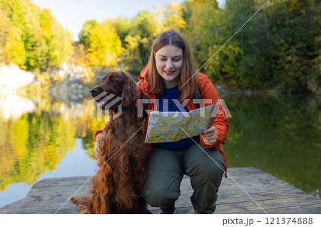 Happy 30s woman hiker hiking in mountain lake. Female with a irish setter dog looking at map and planning trip or get lost.  121374888