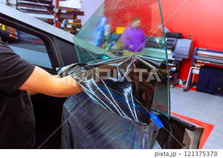 Technician carefully installs window tint film on vehicle in a well equipped work car shop. Technician carefully installs window tint film on vehicle in a well equipped work car shop. 121375378