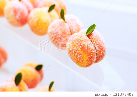 Charming peach shaped sweets are artfully arranged, showcasing blend of orange pink hues with delicate green leaves. Charming peach shaped sweets are artfully arranged, showcasing blend of orange pink hues with delicate green leaves. 121375408