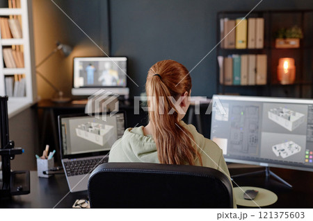 Person with long hair sitting in front of multiple monitors, designing architectural structures in a well-lit office. Background shows organized shelves and modern decor Person with long hair sitting in front of multiple monitors, designing architectural structures in a well-lit office. Background shows organized shelves and modern decor 121375603