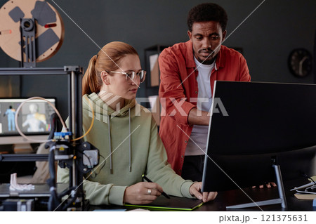 Two colleagues collaborating on project in modern workspace, involving 3D printing and computer workstation, engaging in discussion, sharing ideas, and using technology Two colleagues collaborating on project in modern workspace, involving 3D printing and computer workstation, engaging in discussion, sharing ideas, and using technology 121375631