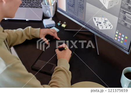 Person creating architectural design on digital graphic tablet with screen showing building layout, surrounded by gadgets and technology on workspace desk 121375659