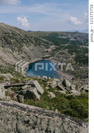 Stone hillsides, evergreen conifers, rocks in distance and emerald colored lake. Summer day in low mountains. Stone hillsides, evergreen conifers, rocks in distance and emerald colored lake. Summer day in low mountains. 121375758