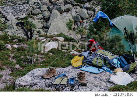 Equipment in the forest: tourist tent, clothes and shoes to dry on tree branches and stones. Tourist camping on a hike. Equipment in the forest: tourist tent, clothes and shoes to dry on tree branches and stones. Tourist camping on a hike. 121375816