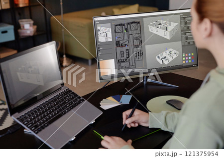 Individual engrossed in creating detailed architectural design on computer using modern digital tools, with another laptop on side for reference and color samples laying on desk 121375954