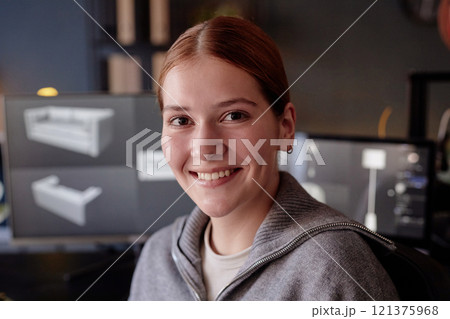 Portrait of woman smiling warmly while working in modern office setting with computer screens displaying design software behind her Portrait of woman smiling warmly while working in modern office setting with computer screens displaying design software behind her 121375968