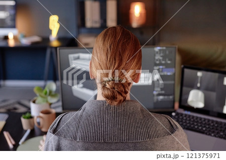 Woman sitting at desk with multiple monitors showing 3D design software in modern office. Professional setting includes organized workspace and soft lighting Woman sitting at desk with multiple monitors showing 3D design software in modern office. Professional setting includes organized workspace and soft lighting 121375971