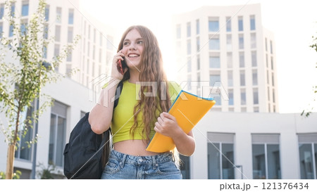 Smiling female student chatting on cellphone on university campus 121376434