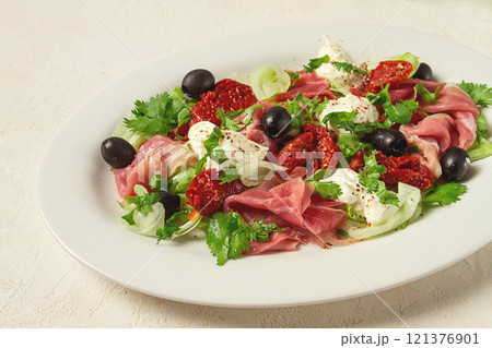 salad with dried tomatoes, prosciutto, soft cheese, olives, homemade, top view, 121376901